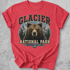 A heather red short-sleeve t-shirt featuring a graphic print of a grizzly bear in Glacier National Park, Montana, with mountains and pine trees in the background.